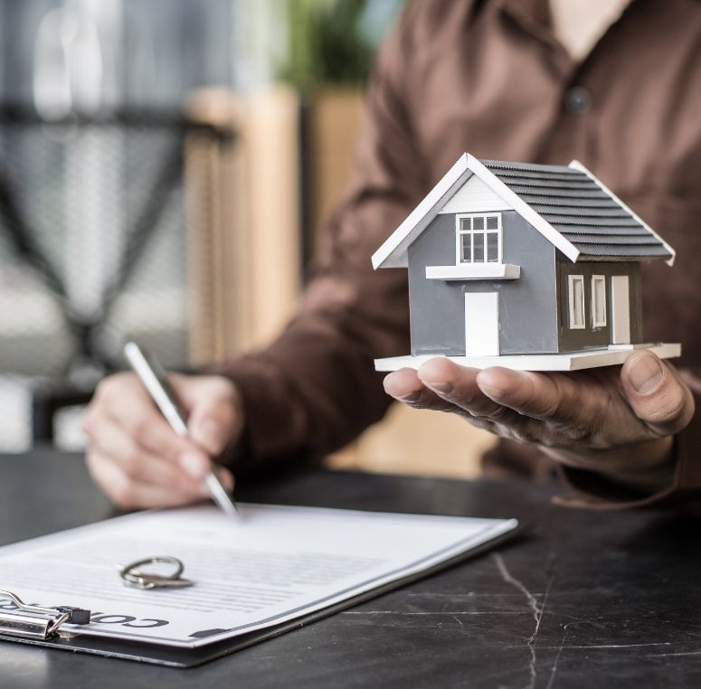 Person holding a model house while signing legal property documents during a settlement