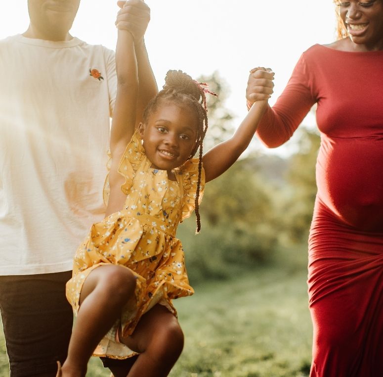 Happy young girl smiling while being lifted by her parents during a sunny outdoor family moment